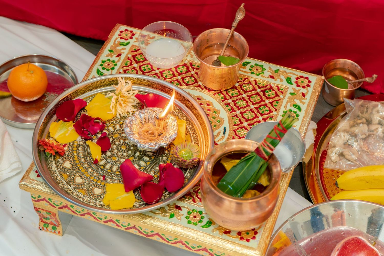 Traditional Hindu puja thali with colorful flowers, copper vessels, and ritual offerings on decorative tray.