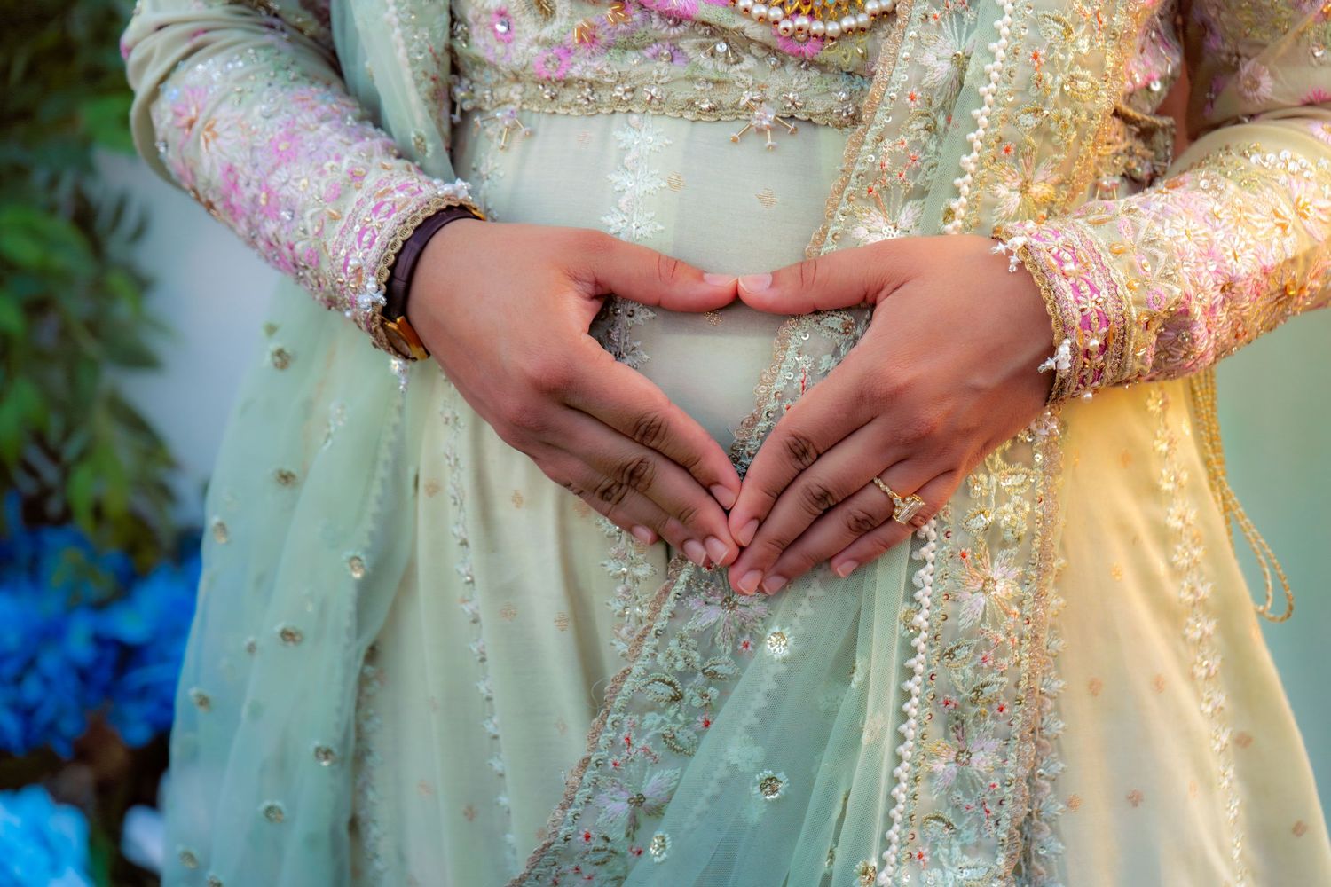 Two people forming a heart shape with their hands over an elegant mint green embroidered Indian bridal outfit.