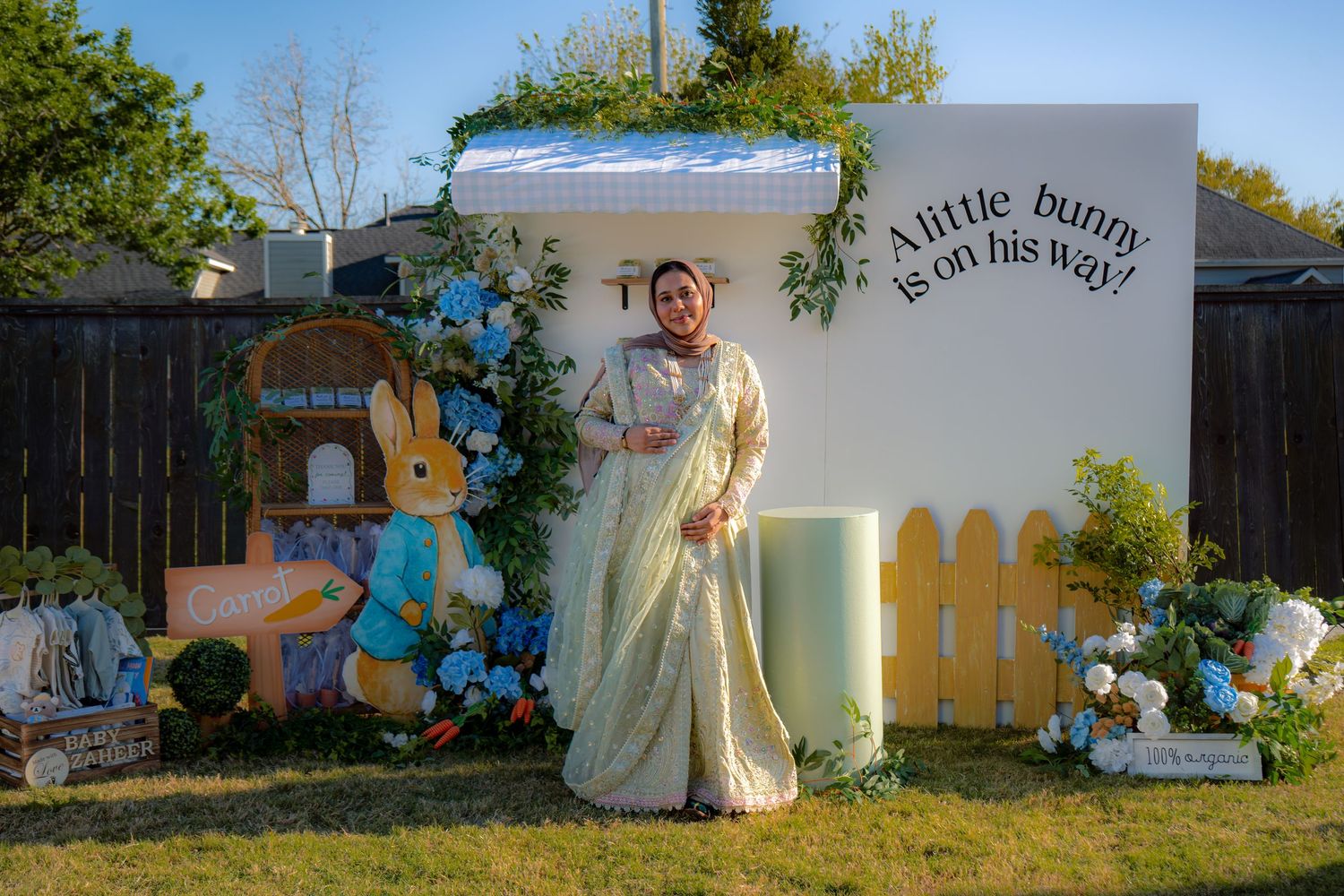 Expectant mother in embroidered saree standing before Peter Rabbit baby shower photo backdrop.