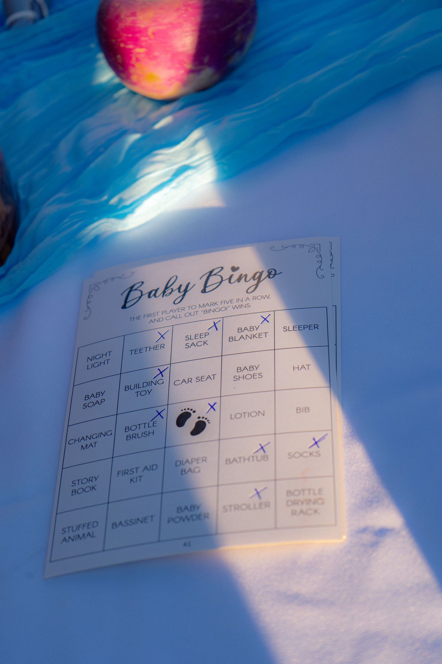 Baby Bingo game card with marked squares placed on a white tablecloth at a shower.