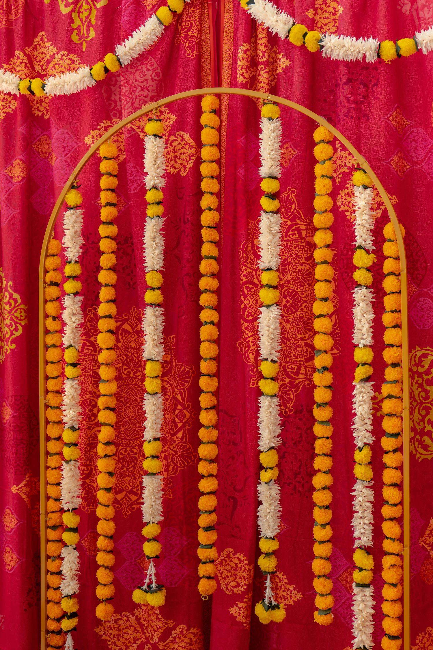 Vibrant Indian wedding decoration with marigold and white flower garlands hanging against a red silk backdrop.