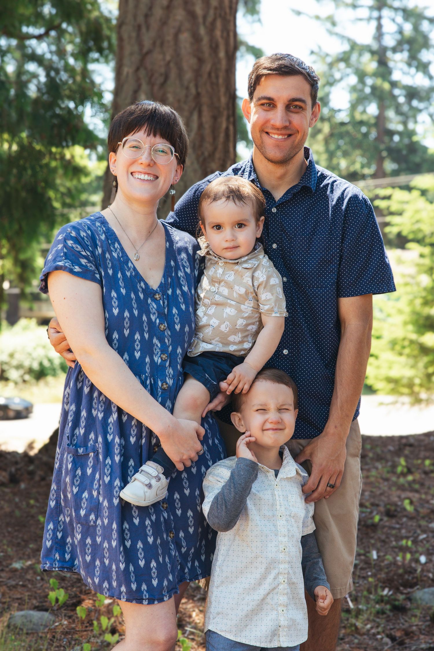 Happy family of four with two young boys smiling in a sunny green park setting.