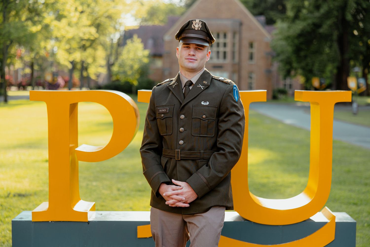 Military officer in dress uniform posing by Pacific Lutheran University sign.