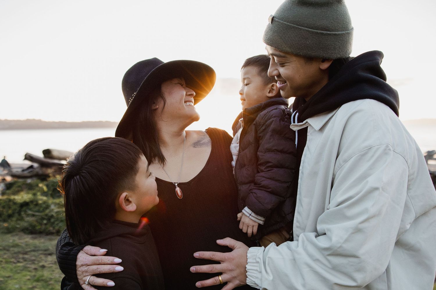 Happy family with two young boys embracing near a scenic waterfront at golden hour.