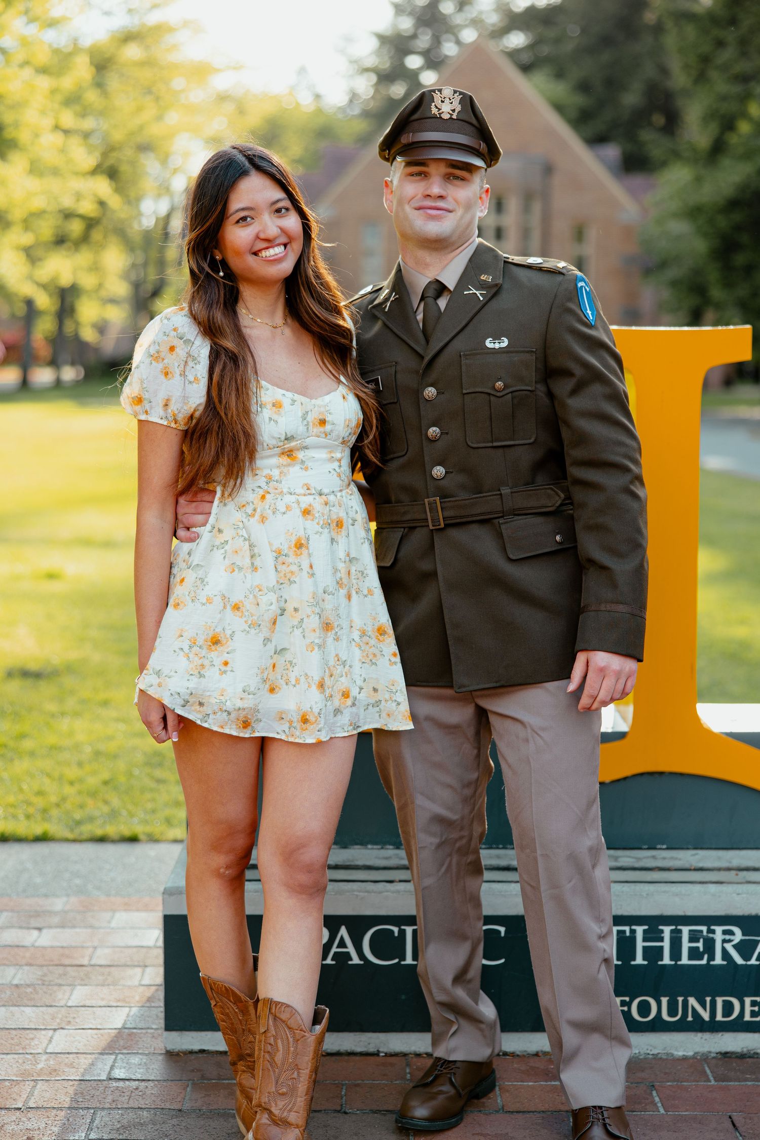 Smiling couple posing by Pacific Lutheran University sign, man in Army dress uniform beside woman in floral dress.