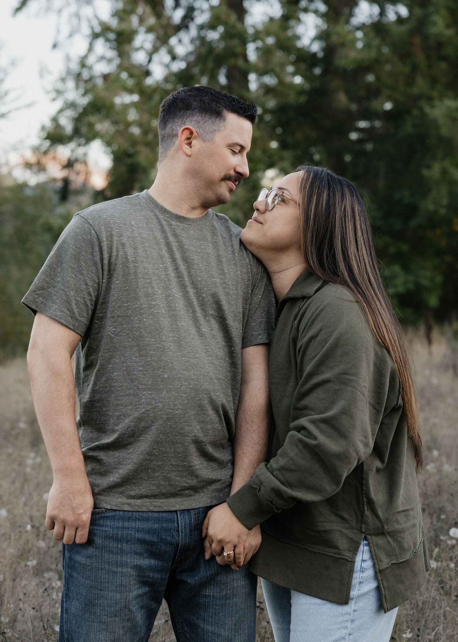 Couple holding hands and gazing at each other lovingly in a natural outdoor setting.