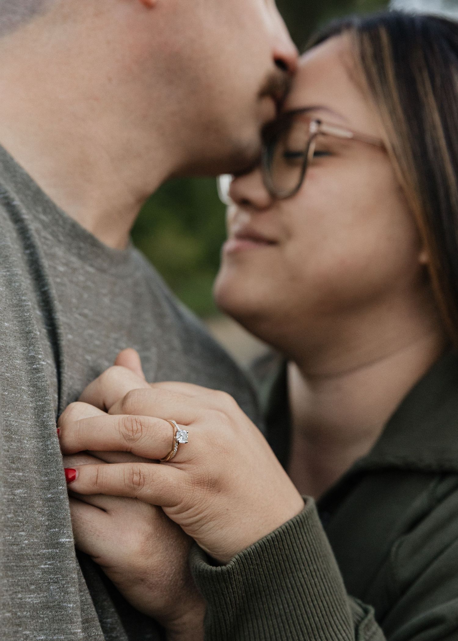 Close-up of couple nearly kissing with woman displaying her diamond engagement ring.