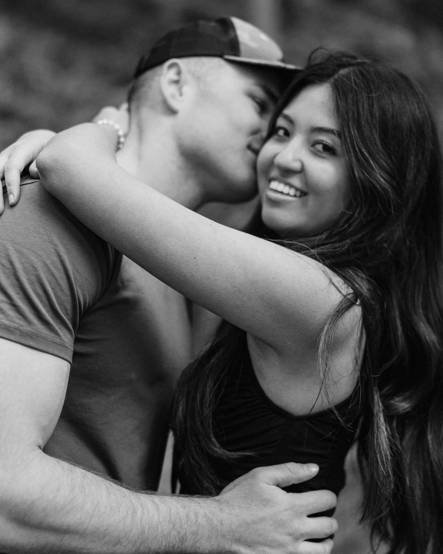 A couple shares a romantic moment outdoors, man kissing woman's cheek as she smiles, black and white photo.