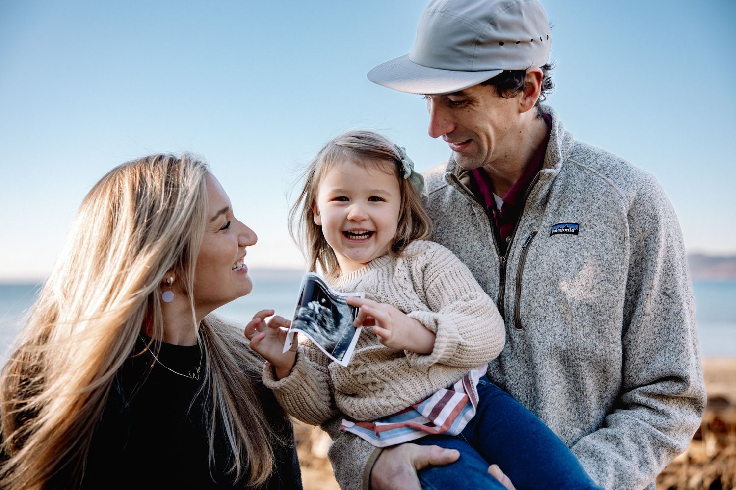 Happy family of three shares pregnancy announcement with ultrasound at beach.