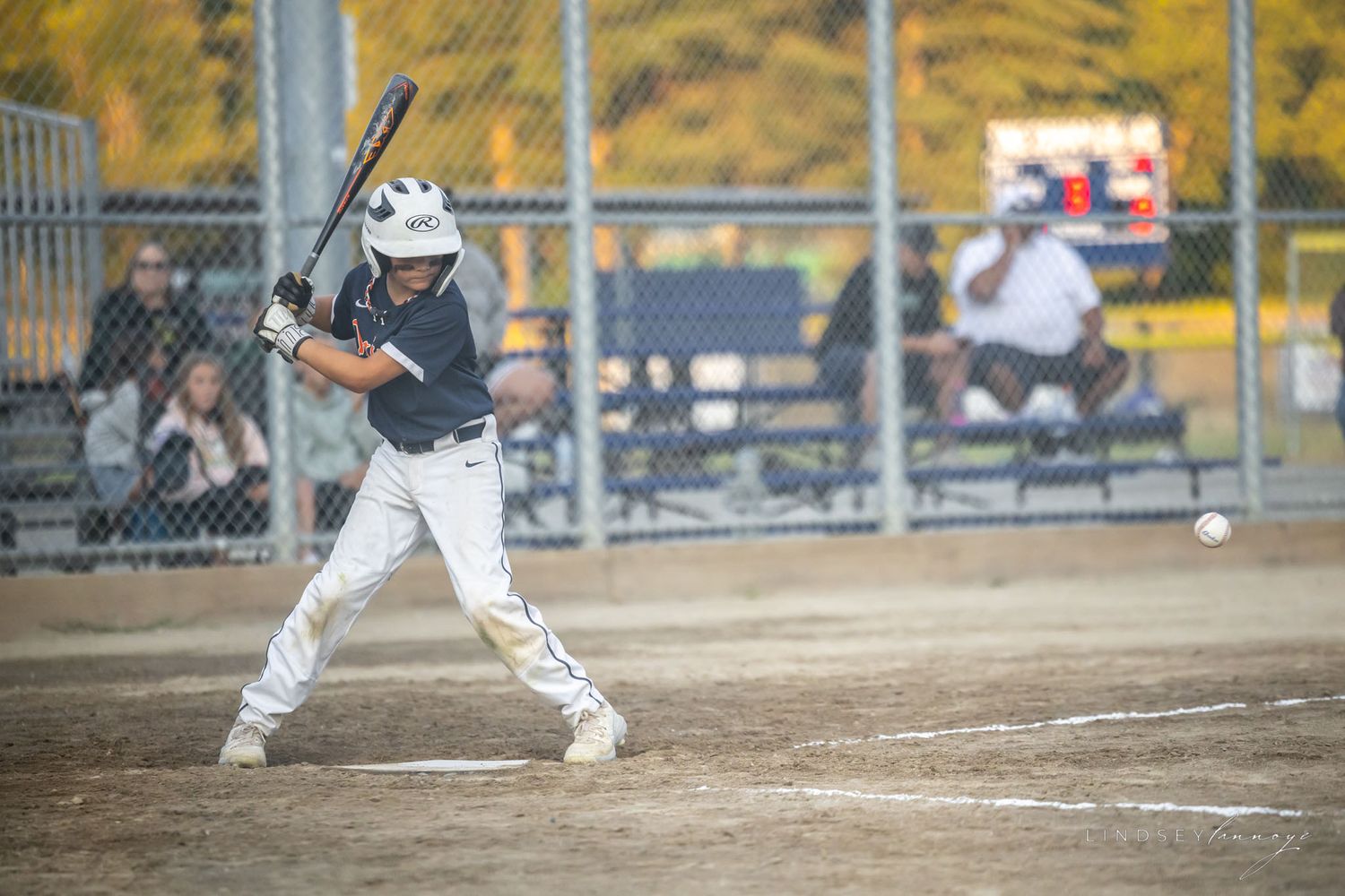 Young baseball player in white uniform swings at a pitch during an outdoor youth league game.