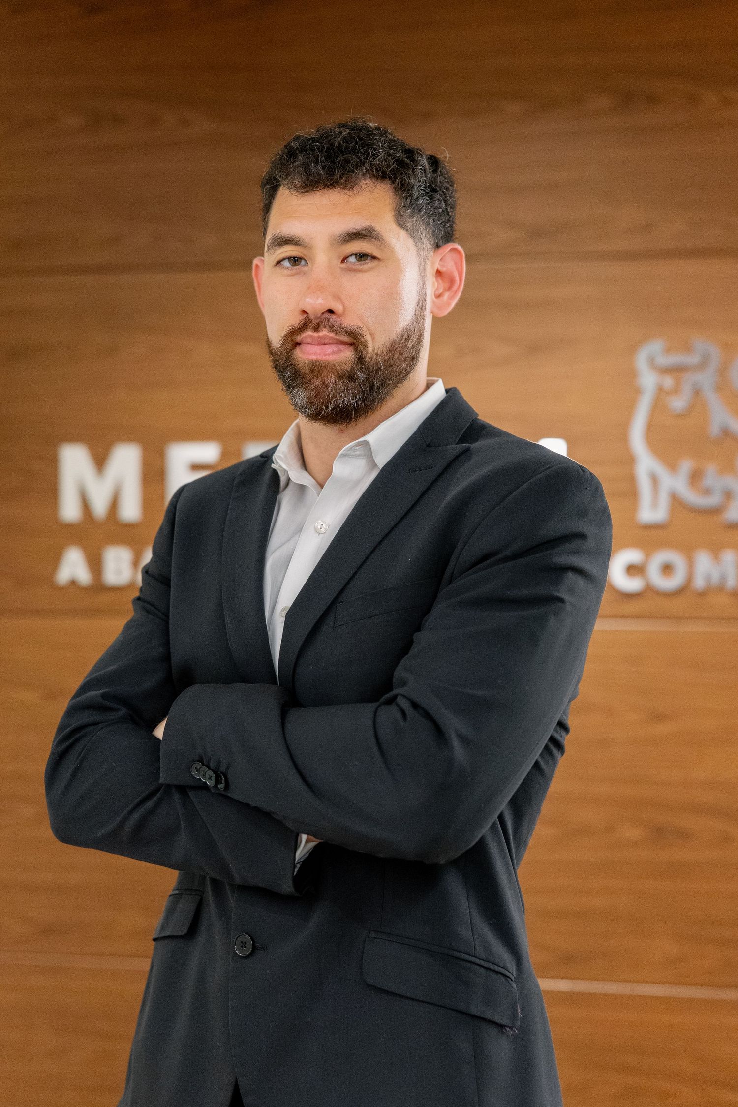 Professional bearded man in dark blazer posing with arms crossed before Merrill Lynch logo.