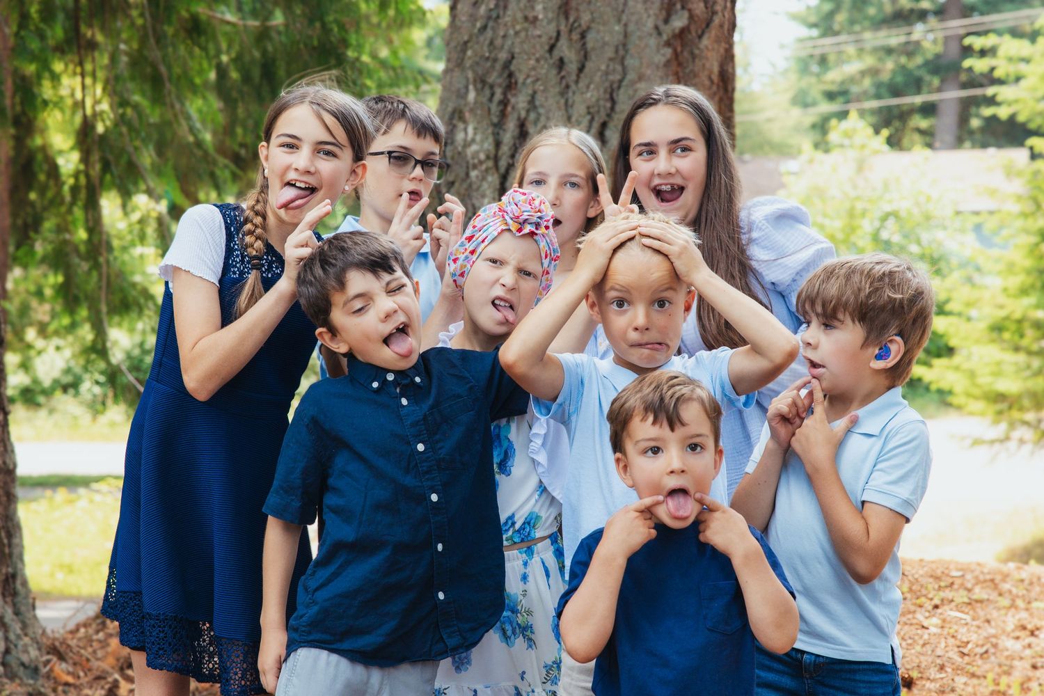 Group of excited children making funny faces outdoors near a large tree during a family photo session.