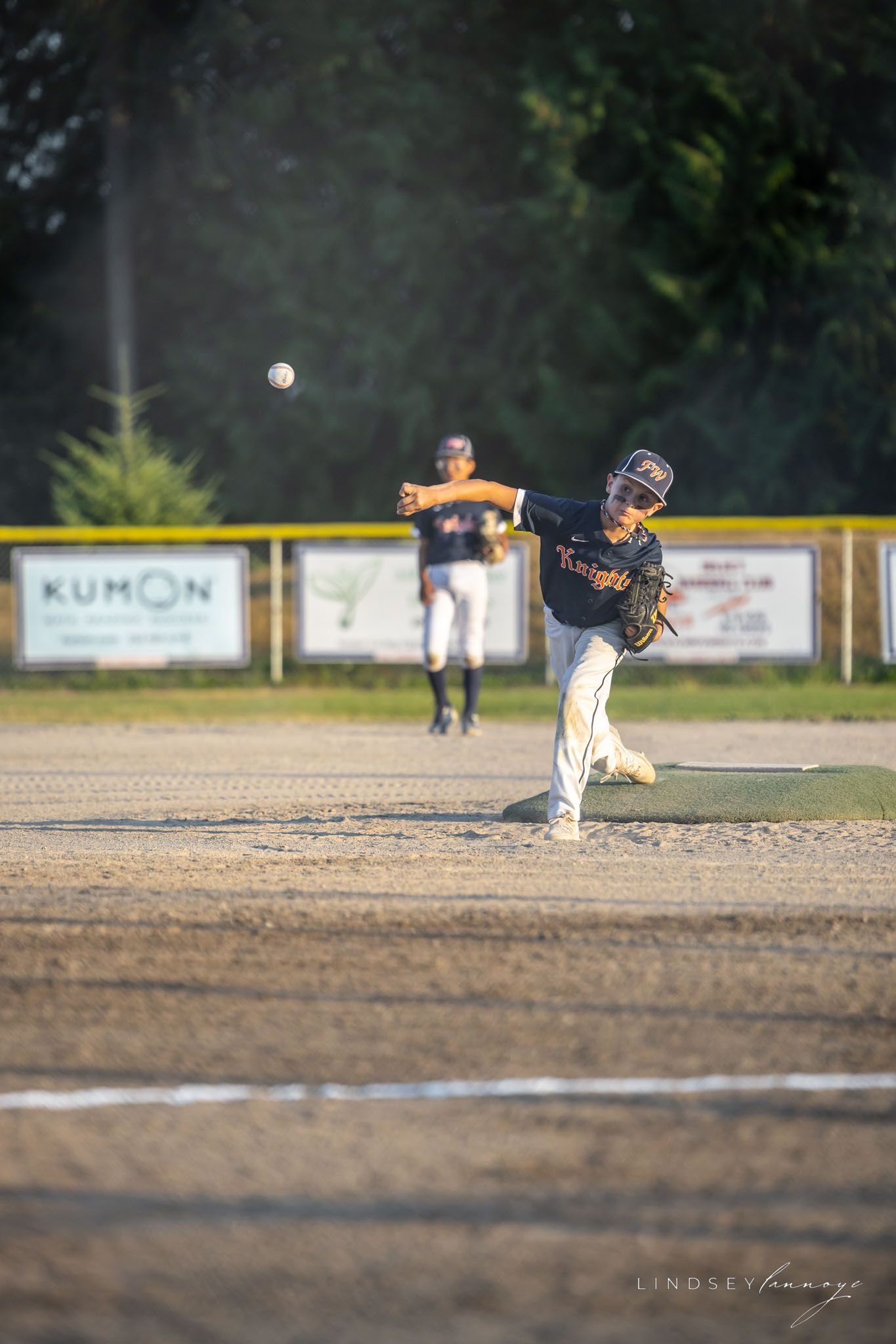 Youth baseball pitcher in Knights uniform delivers a pitch during an evening little league game.