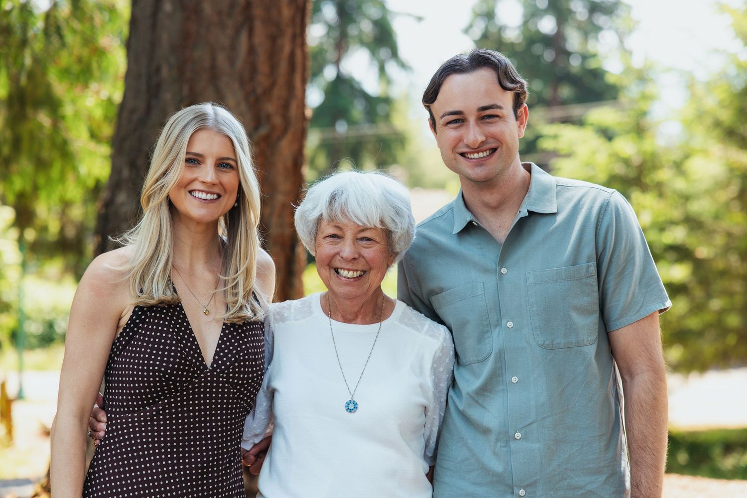 Senior woman posing with young adult man and woman outdoors in sunny park.