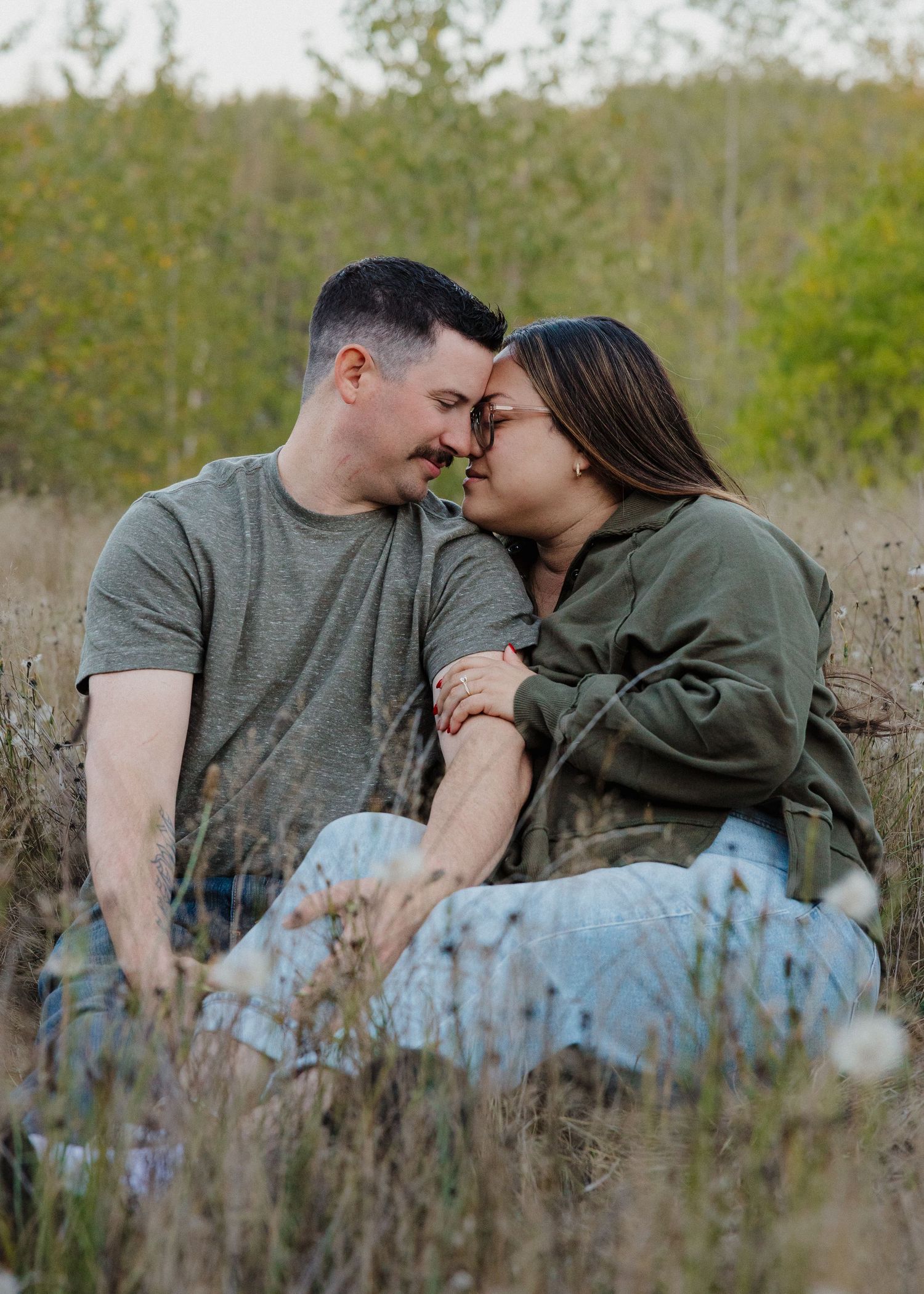 Couple sitting in a field leaning foreheads together romantically during an outdoor engagement photo session.