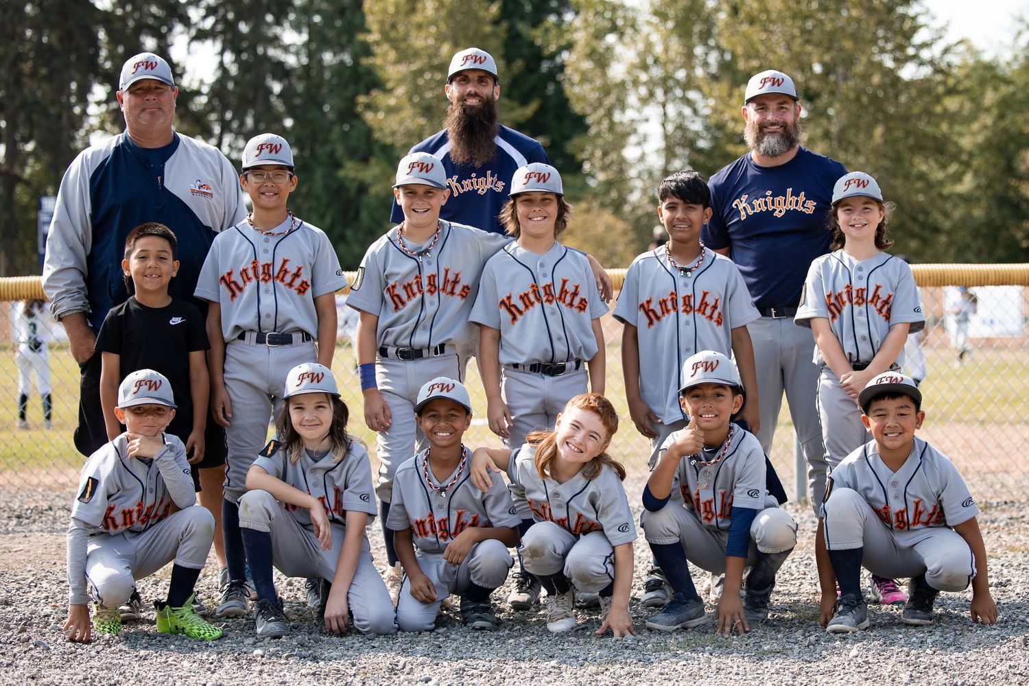 Youth Knights baseball team poses for a group photo in gray uniforms on a sunny day at the baseball field.