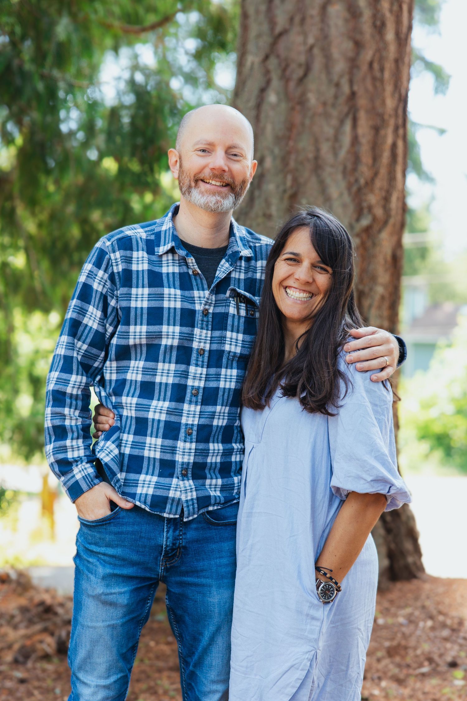 Smiling couple posing together outdoors near a large tree trunk.