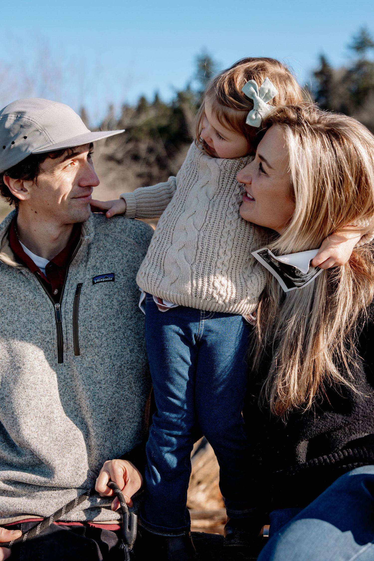 Parents and toddler share a tender moment together outdoors on sunny day.