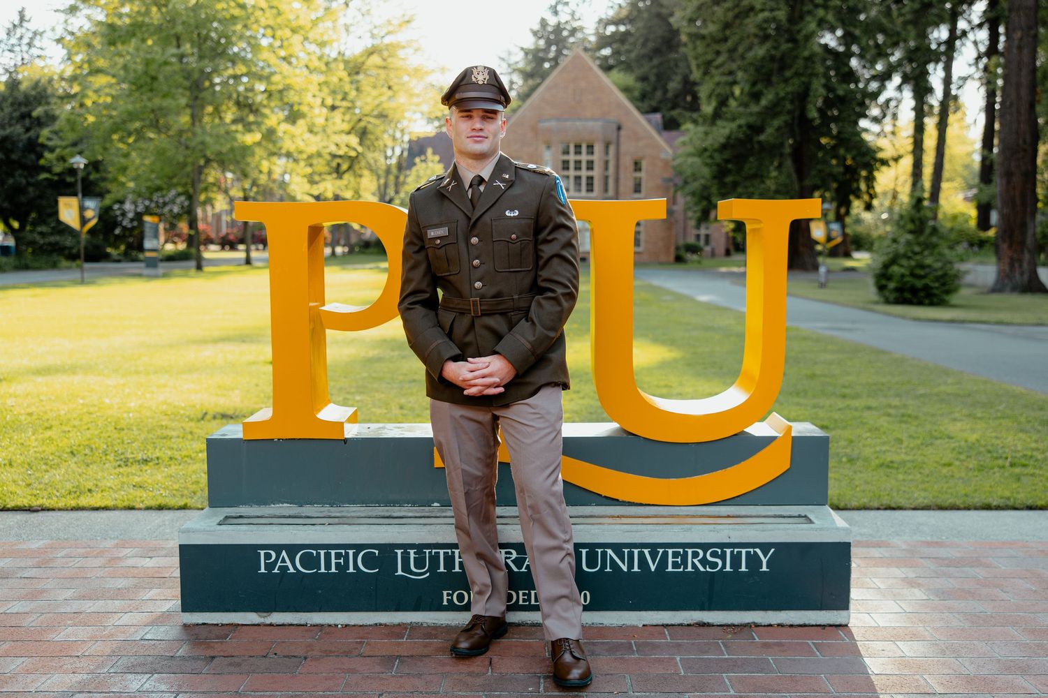 Student in military uniform standing before Pacific Lutheran University sign on campus.