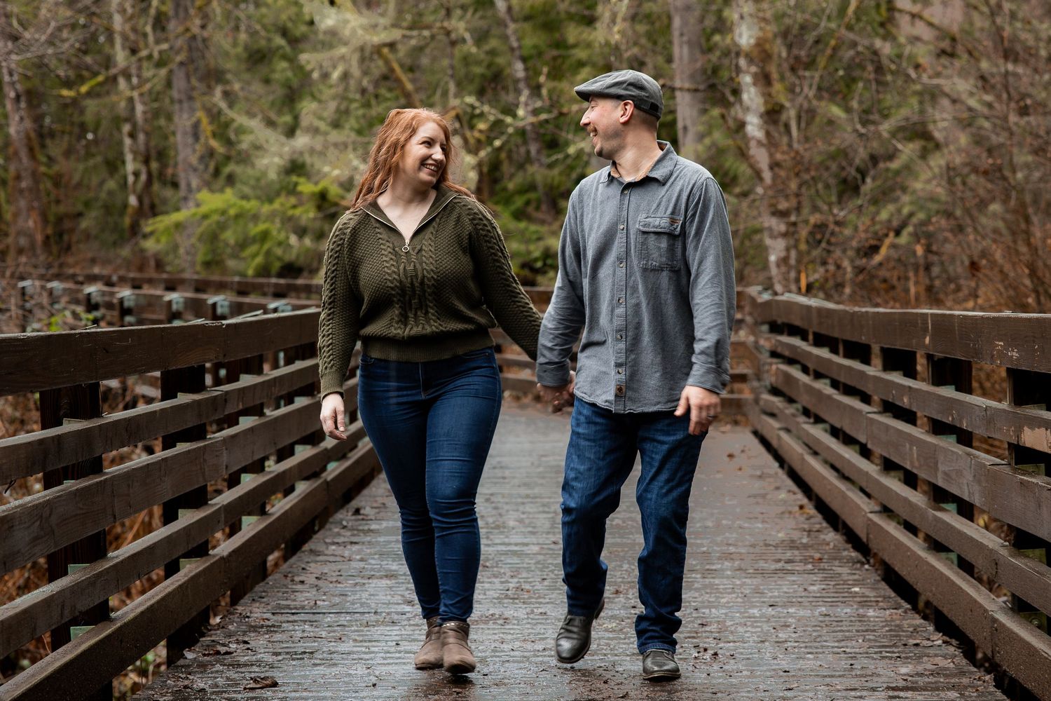 Couple holding hands and walking together on a wooden bridge in a rainy forest.