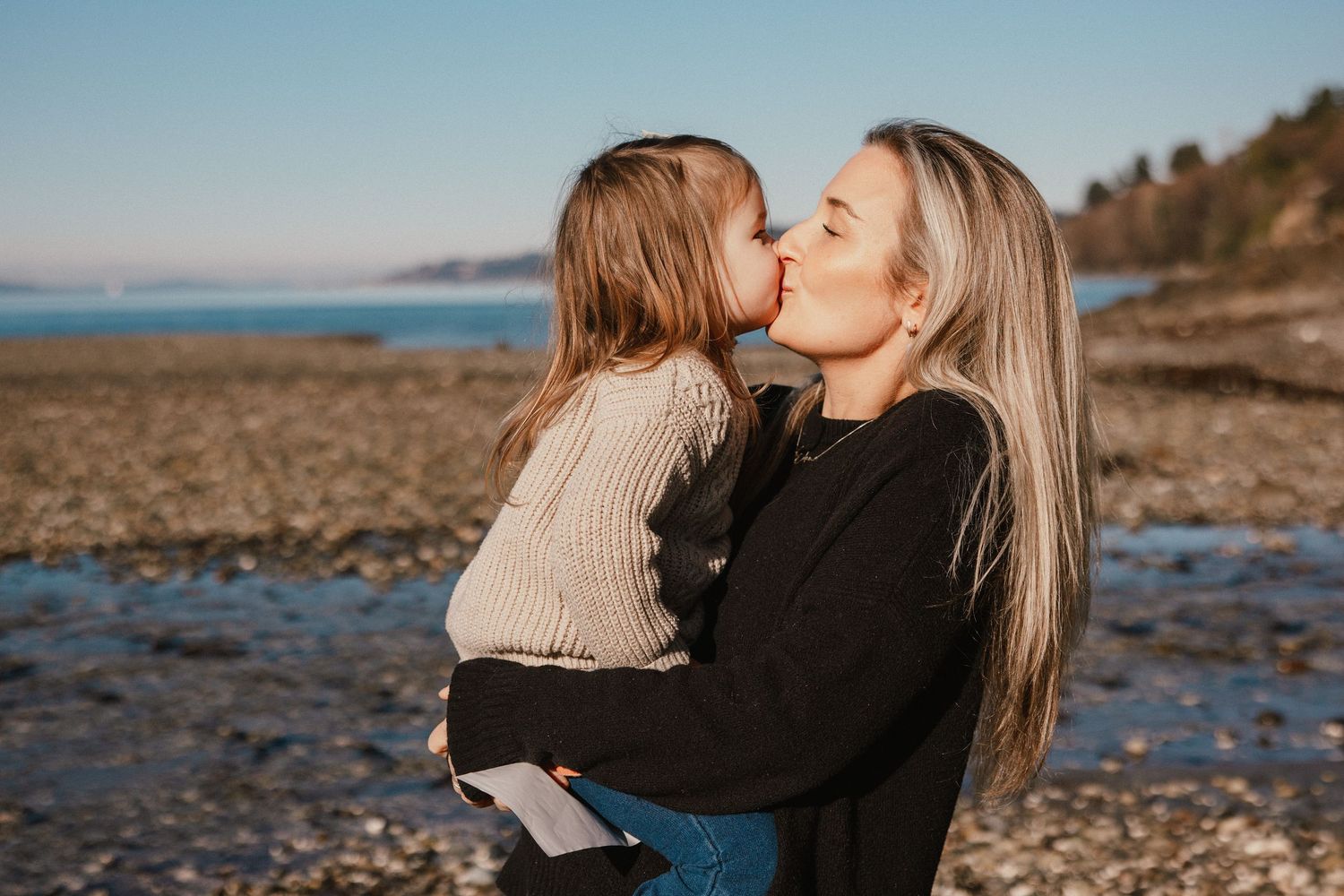 Mother and toddler daughter share a sweet kiss on the beach.
