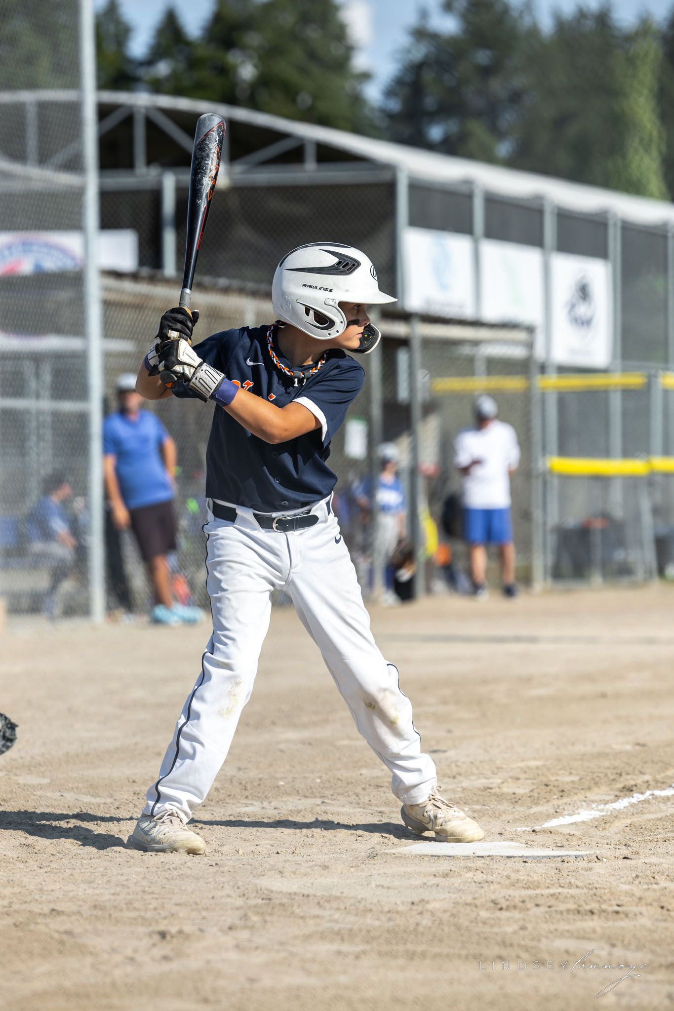 Youth baseball player in navy uniform and white helmet stands ready to bat during a sunny day game.