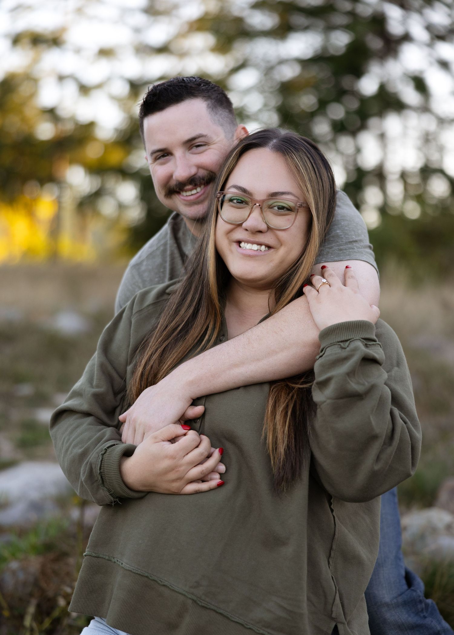 Happy couple embracing outdoors, woman wearing green hoodie and glasses smiling at camera.
