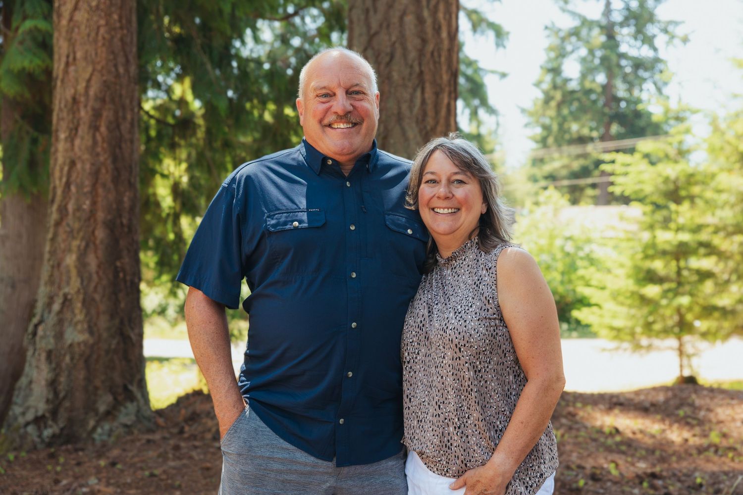 Happy couple posing together outdoors among tall trees on a sunny day.