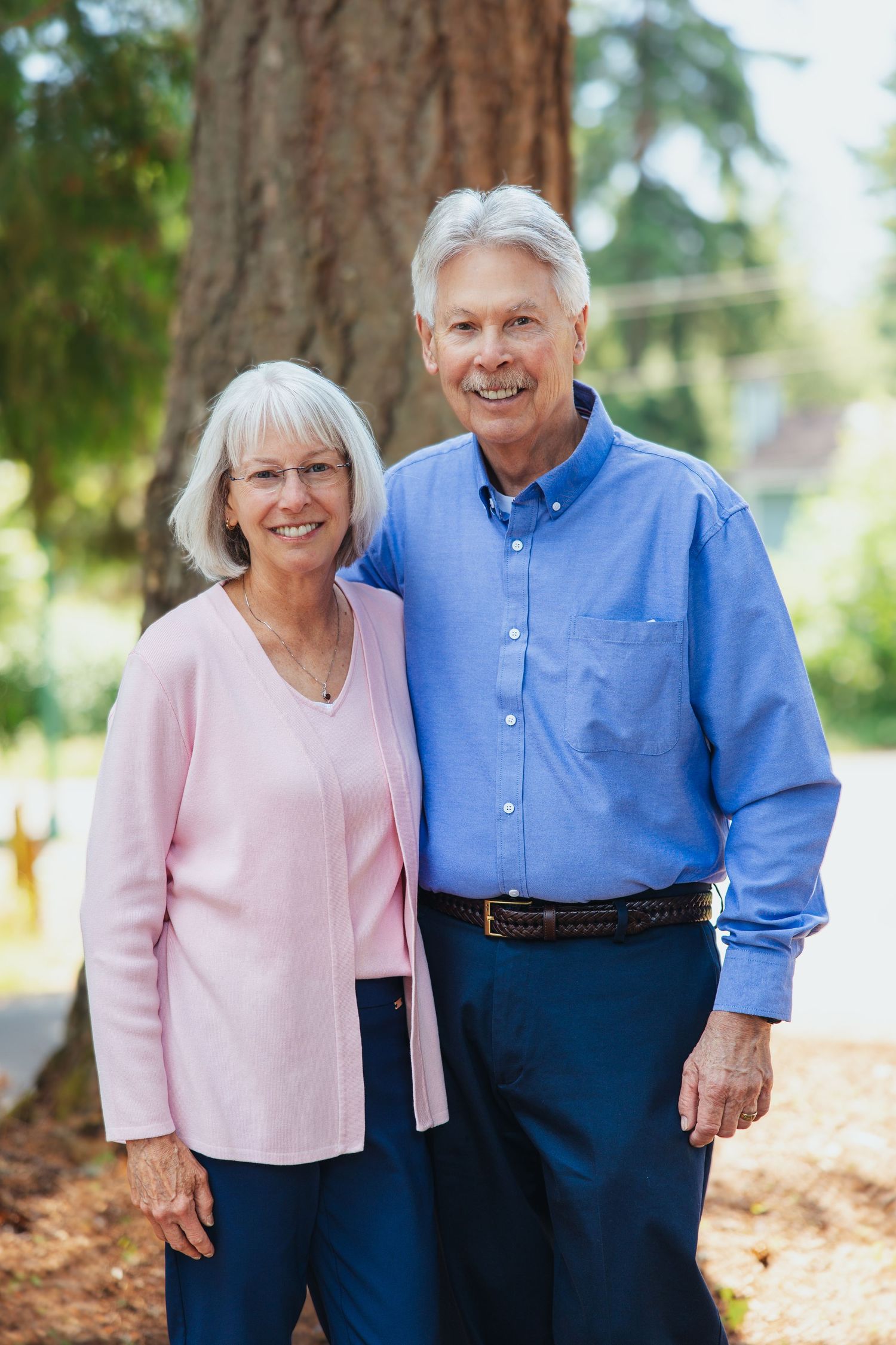 Smiling senior couple posing together outdoors in a sunny park setting.