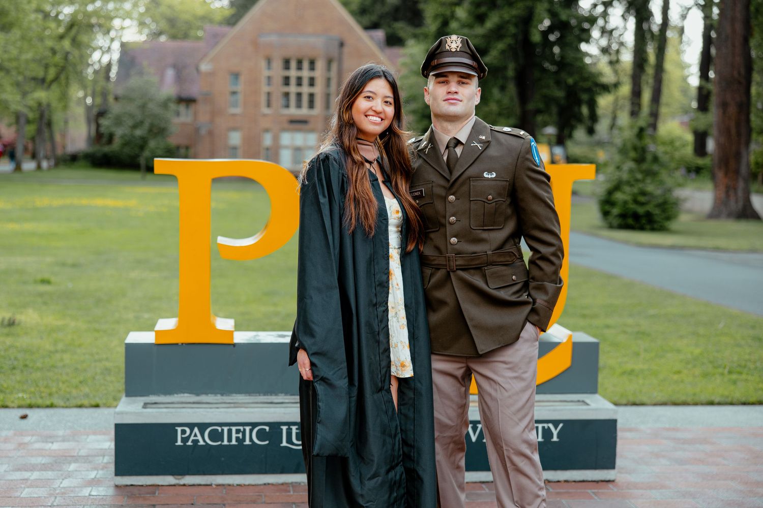 Couple posing at Pacific Lutheran University graduation, woman in green gown and man in military dress uniform.