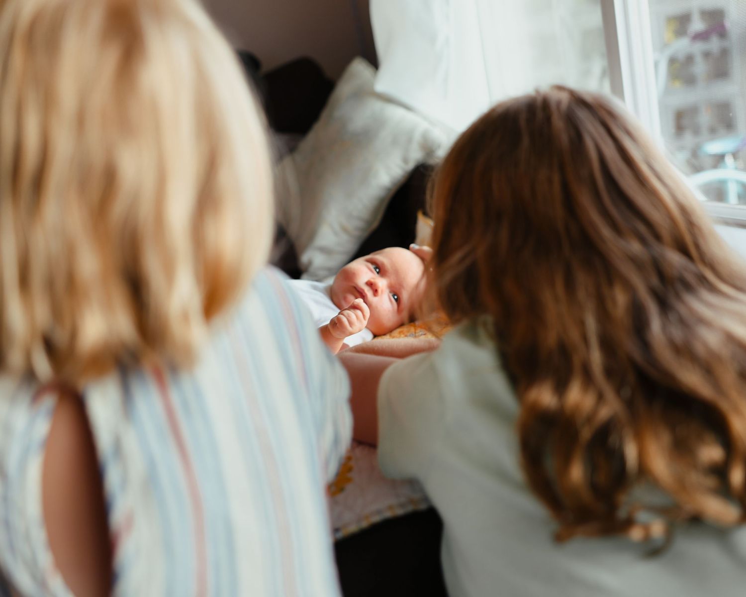 Two children with blonde and brown hair leaning over to look at sleeping newborn baby.