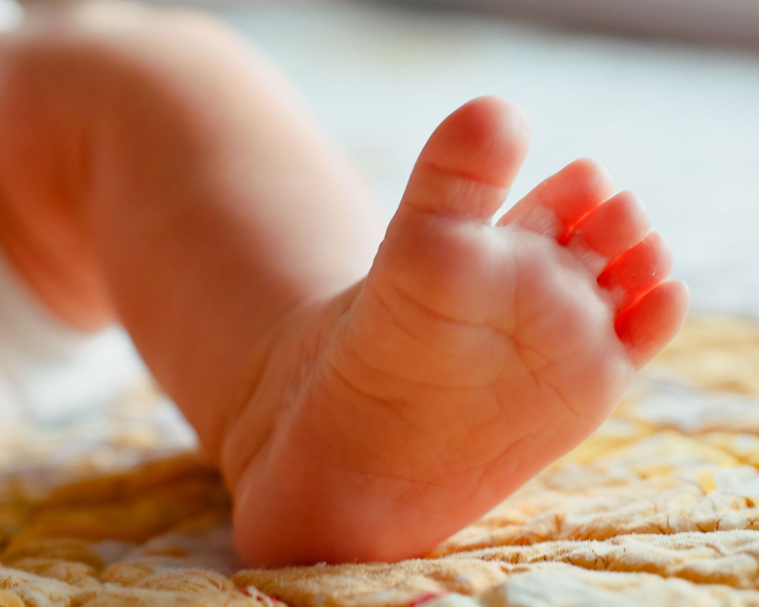 Close-up of tiny newborn baby foot resting on soft yellow quilted blanket.