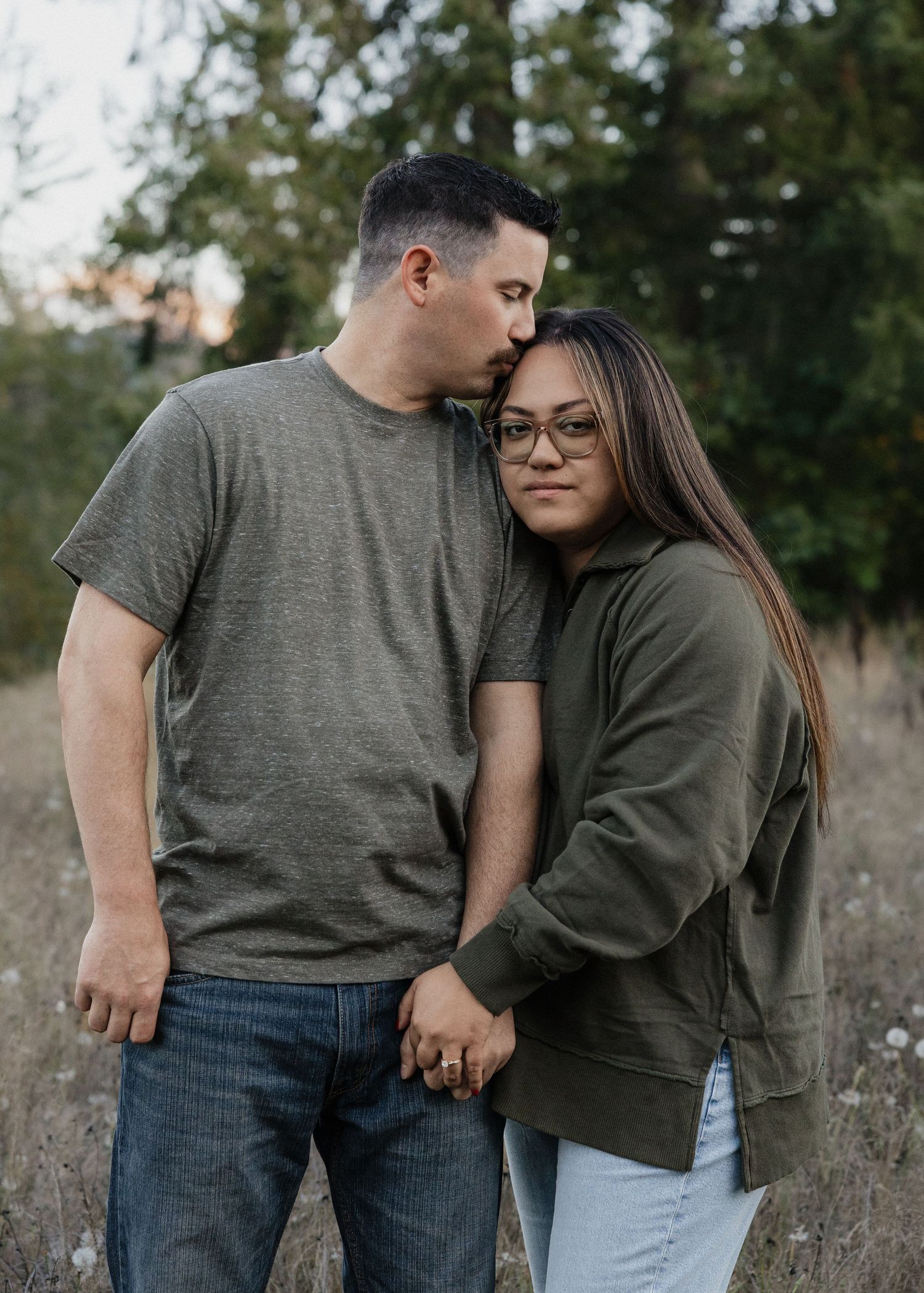Couple holding hands in a field, man tenderly kissing woman on the head.