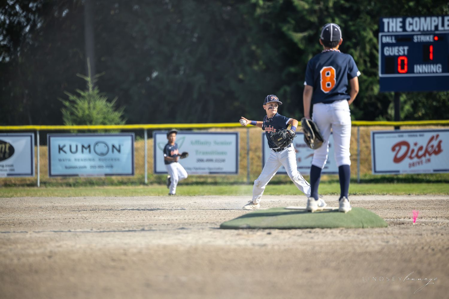 Young baseball players in navy uniforms play defense at second base during a youth league game.
