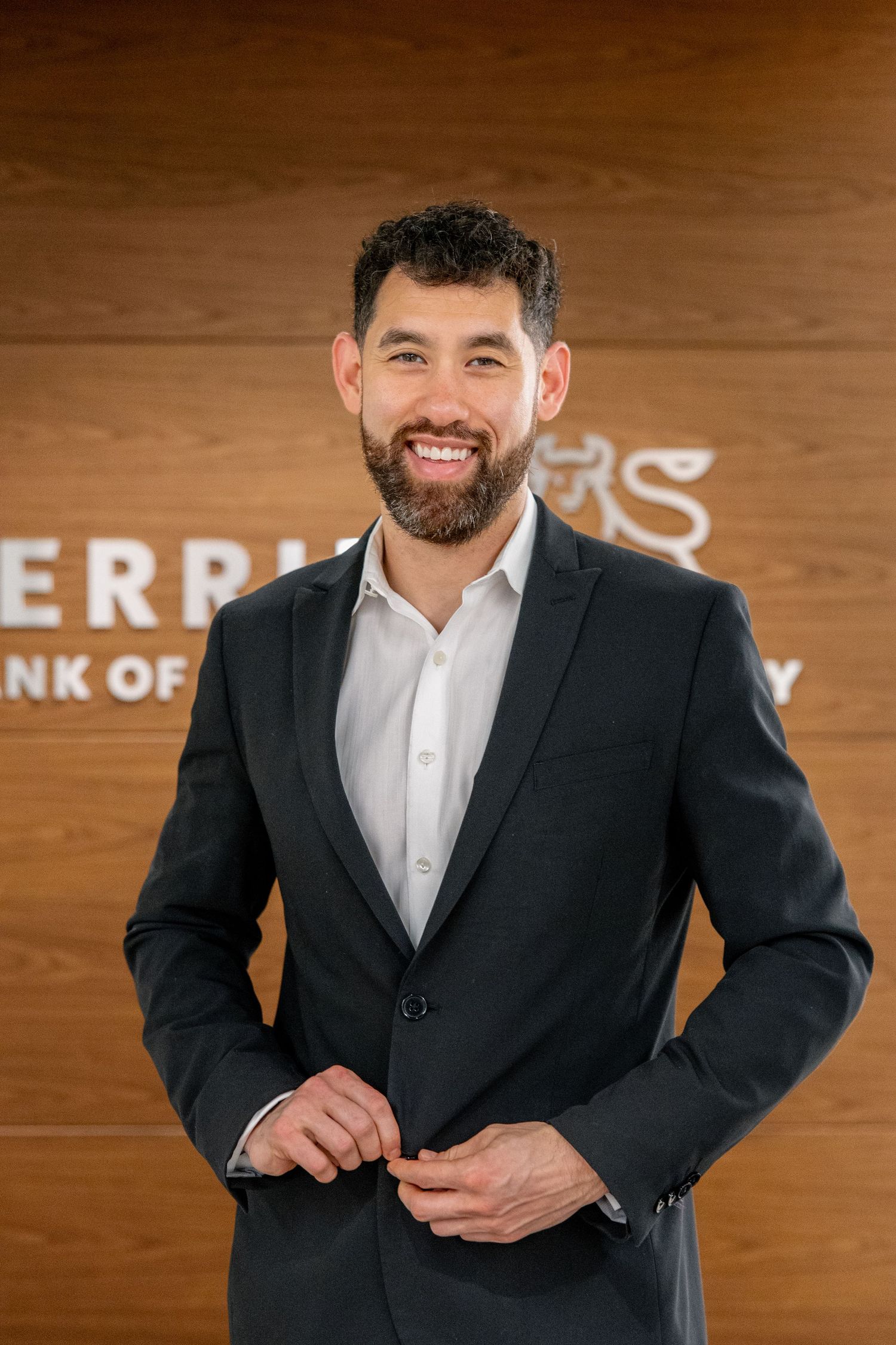 Professional bearded man in dark suit smiling in front of Merrill Lynch office sign.
