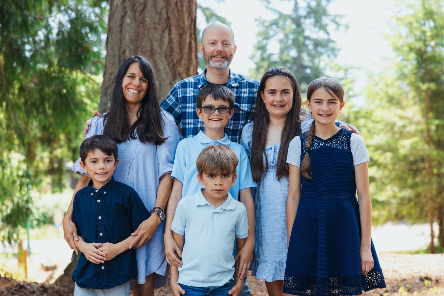 Family of seven posing together in a sunny wooded outdoor setting.