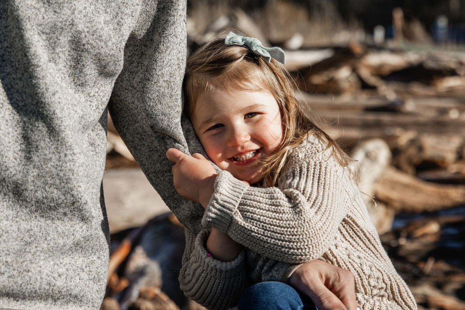 Smiling little girl in knit sweater holds adult's hand outdoors.