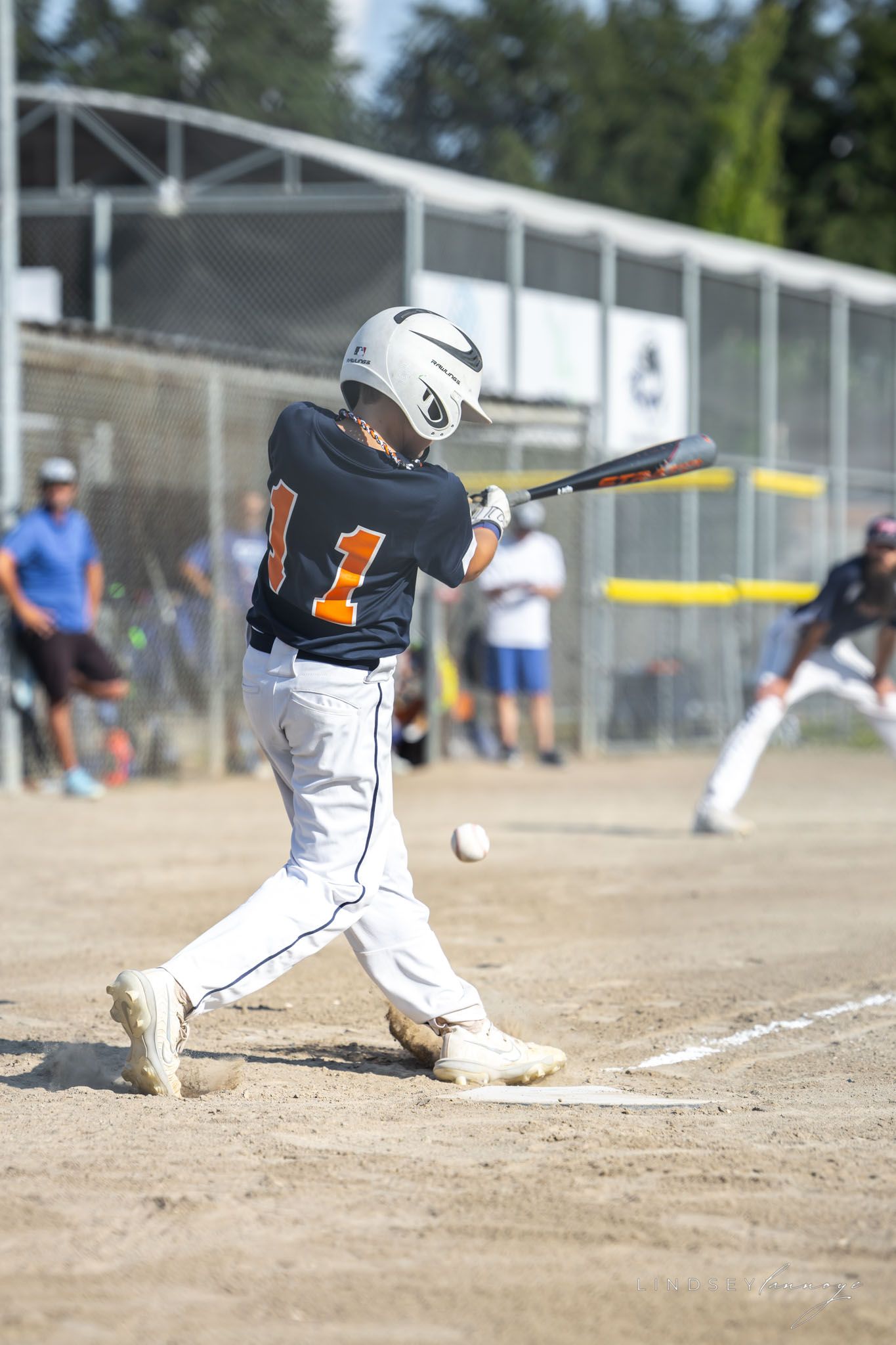 Youth baseball player wearing number 1 swings bat making contact with ball during a competitive game.