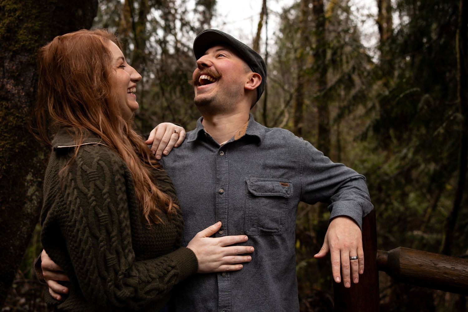 Joyful couple laughing together outdoors in a lush green forest setting.
