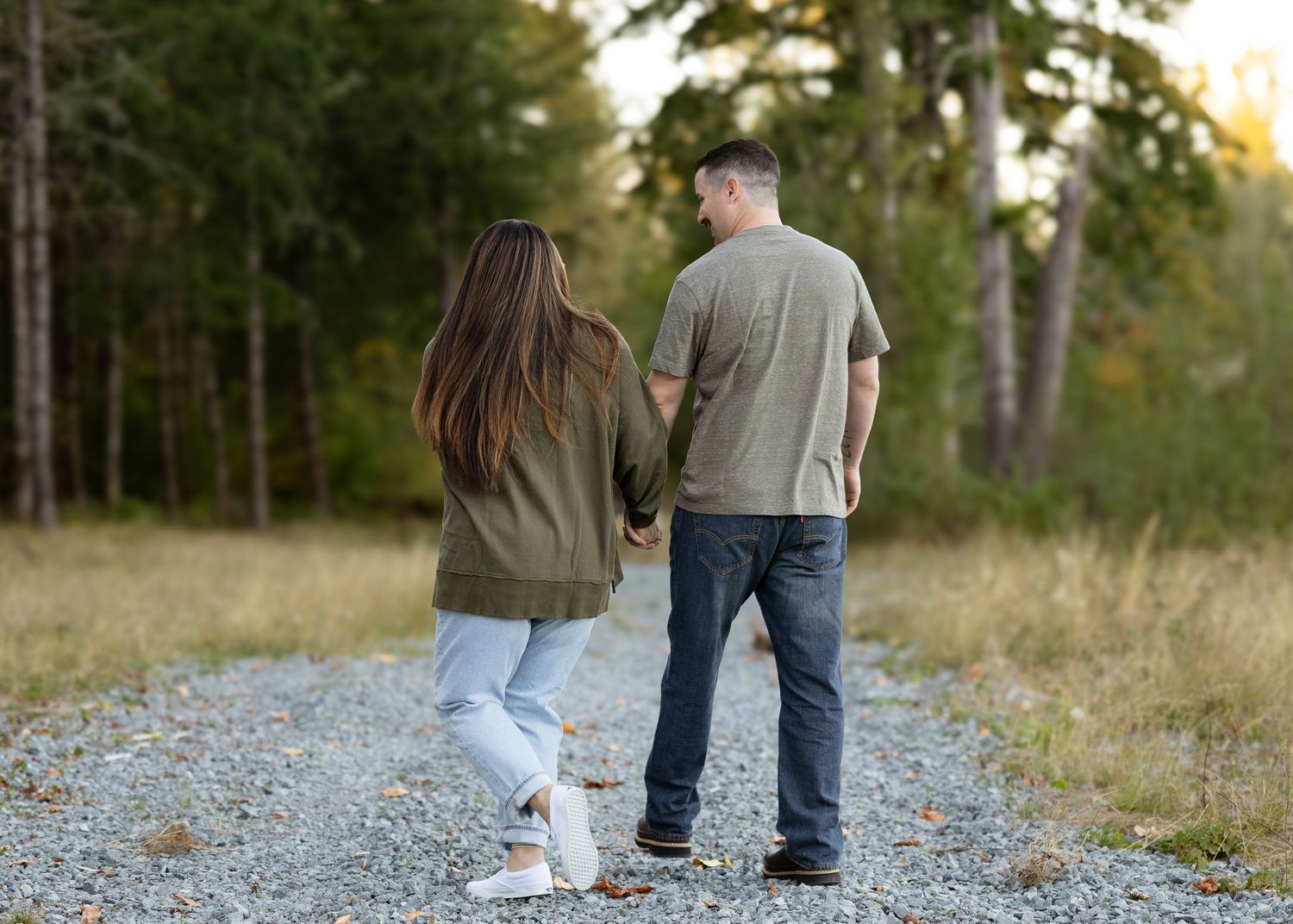 Couple walking hand-in-hand down a gravel path surrounded by lush green forest.
