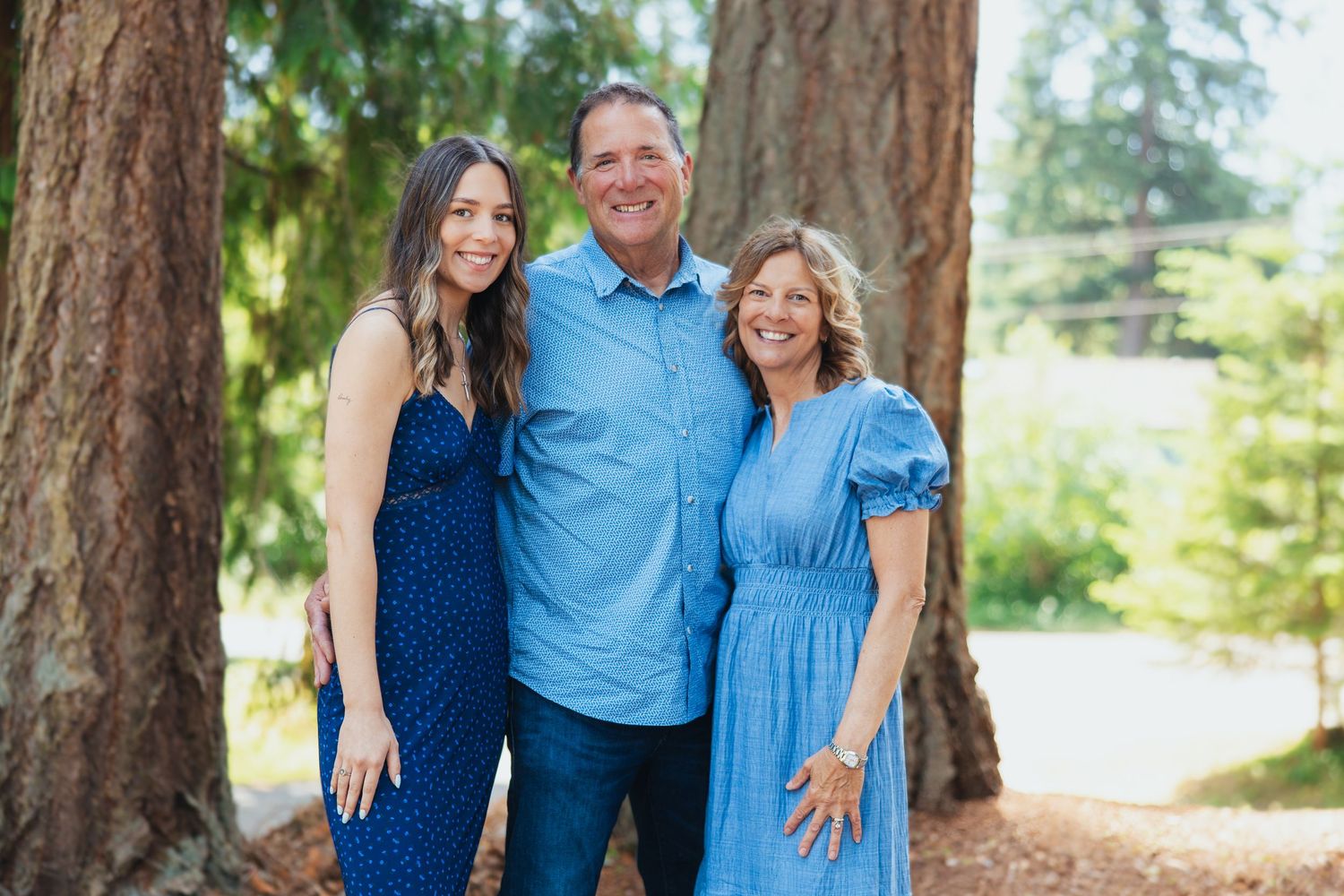 Smiling trio in blue outfits posing outdoors near tall trees.