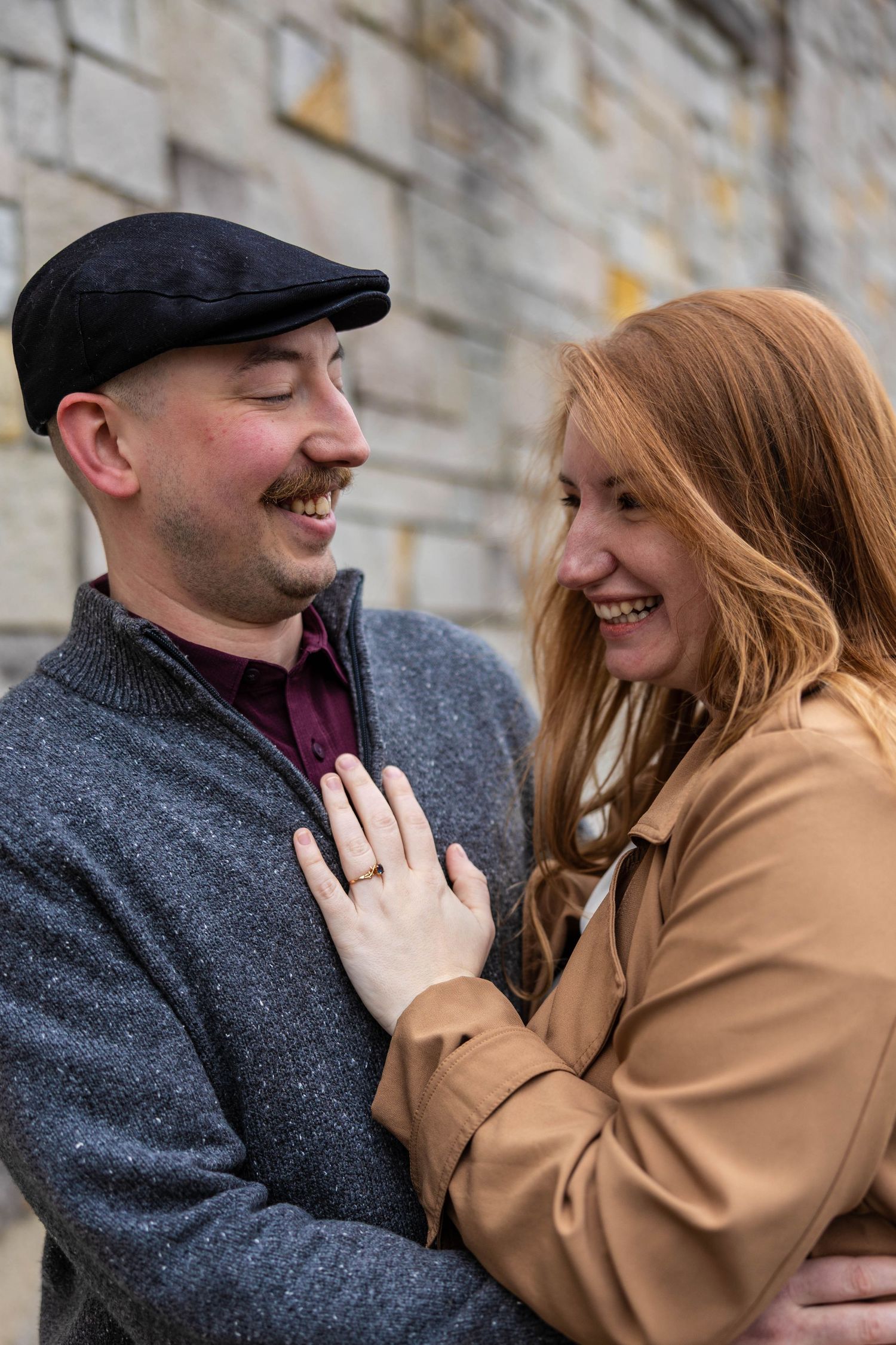 Laughing couple sharing a joyful moment outdoors, woman with red hair placing hand on mans grey sweater.