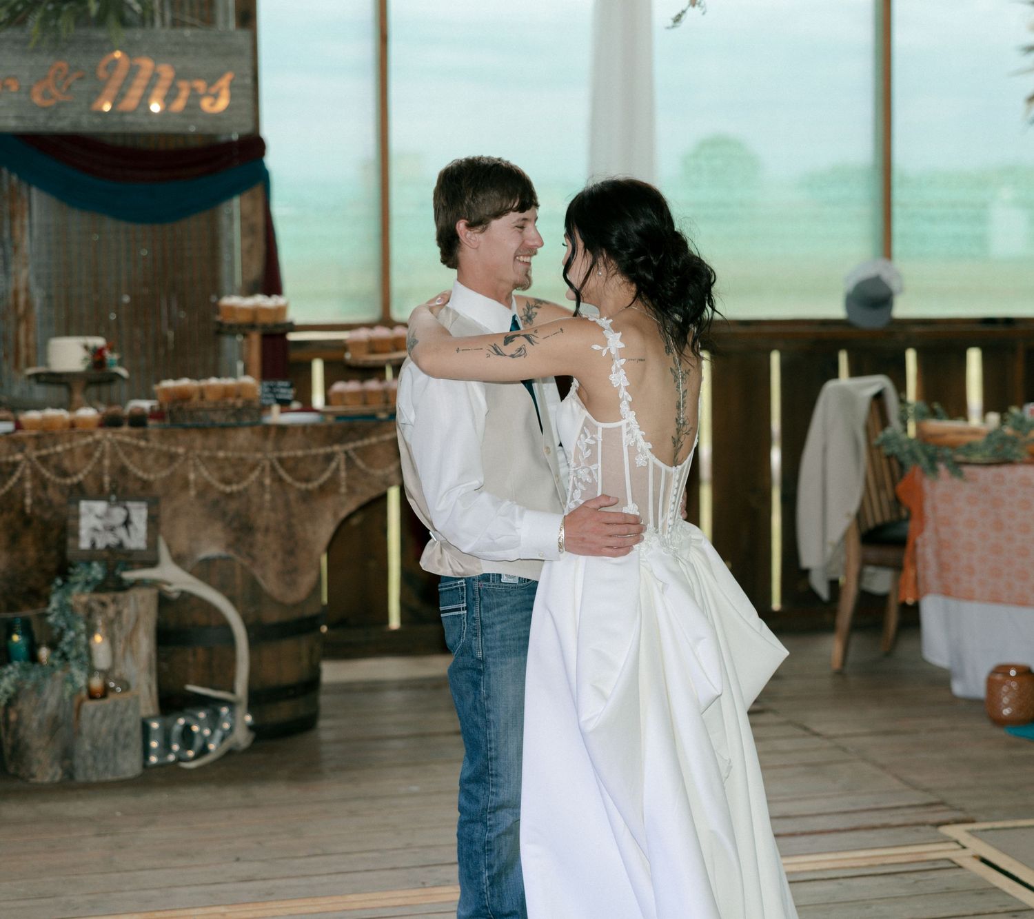 Bride and groom share their first dance in a rustic barn wedding venue with decorated tables in the background.