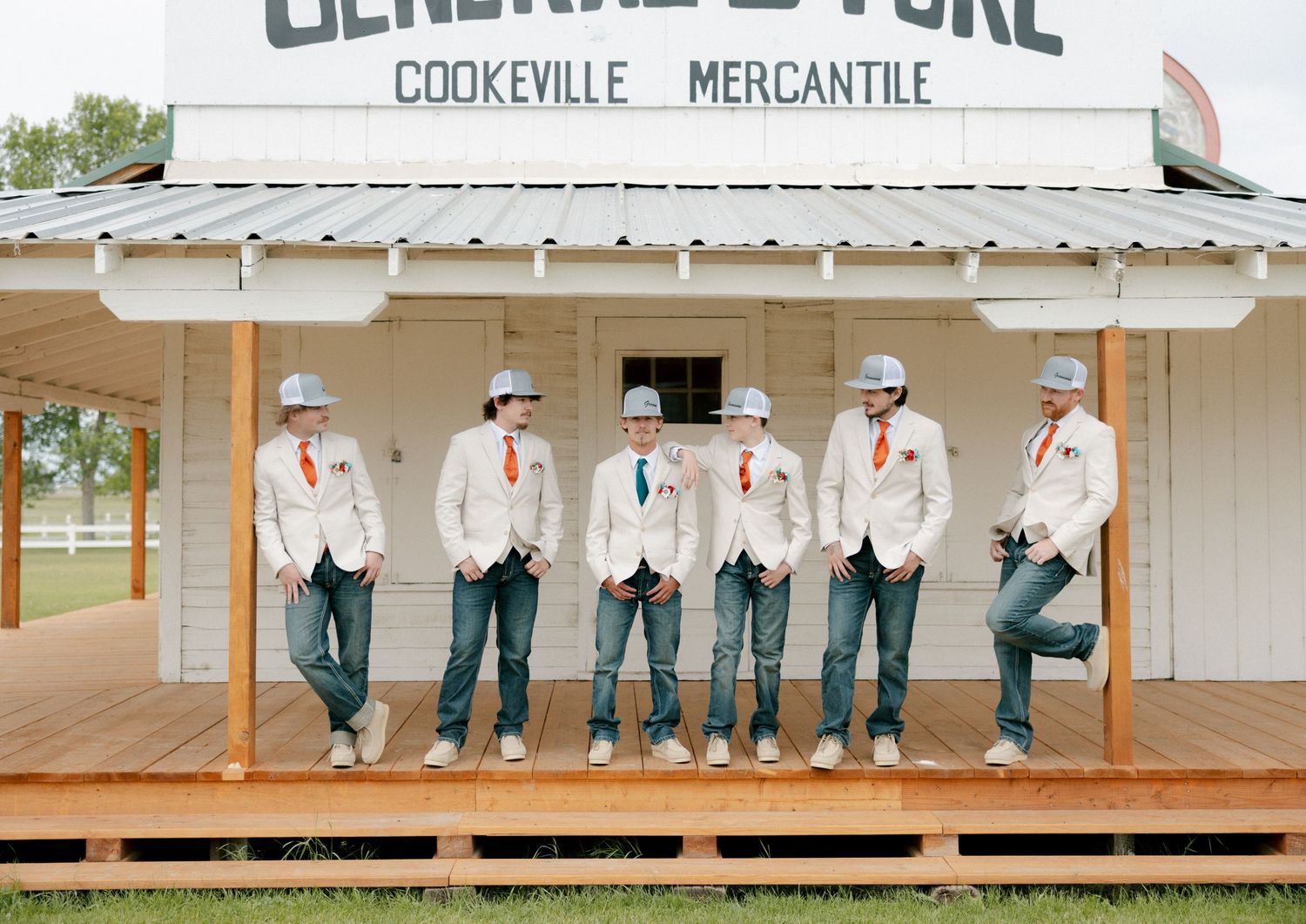 Six groomsmen in tan blazers, jeans, and hard hats pose on a wooden porch at Cookeville Mercantile General Store.