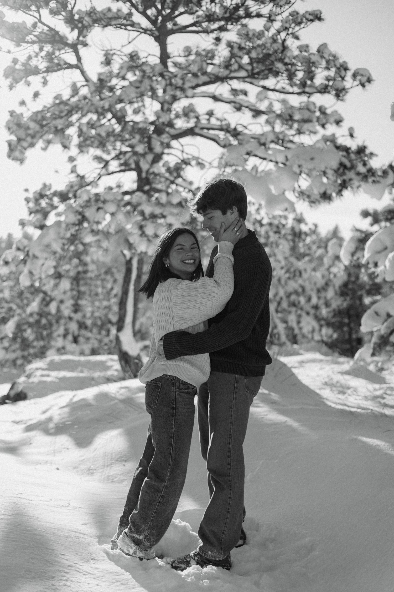Black and white photo of couple embracing and laughing in snowy winter landscape.