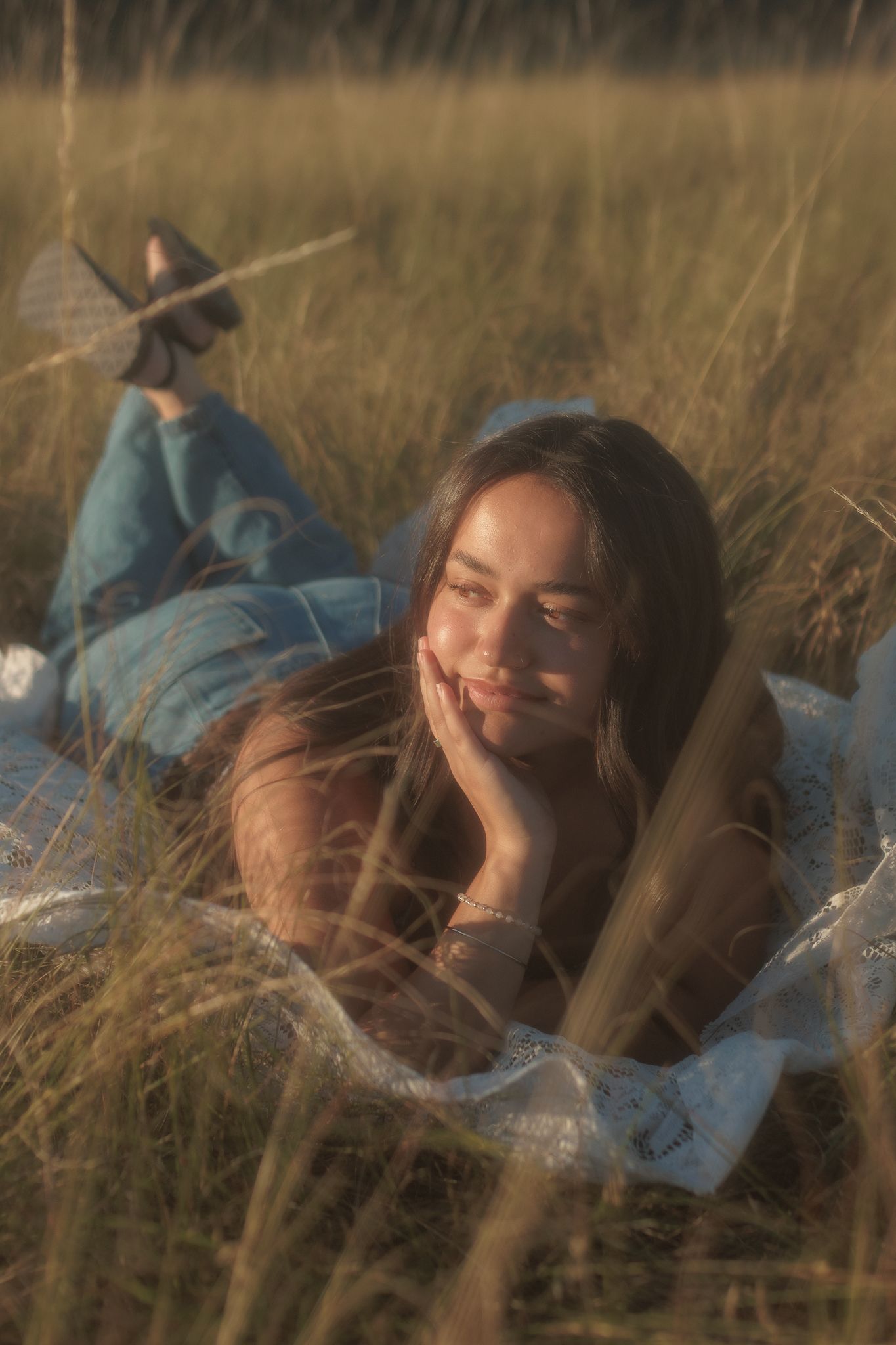 Young woman lying in golden tall grass field during warm sunset light.