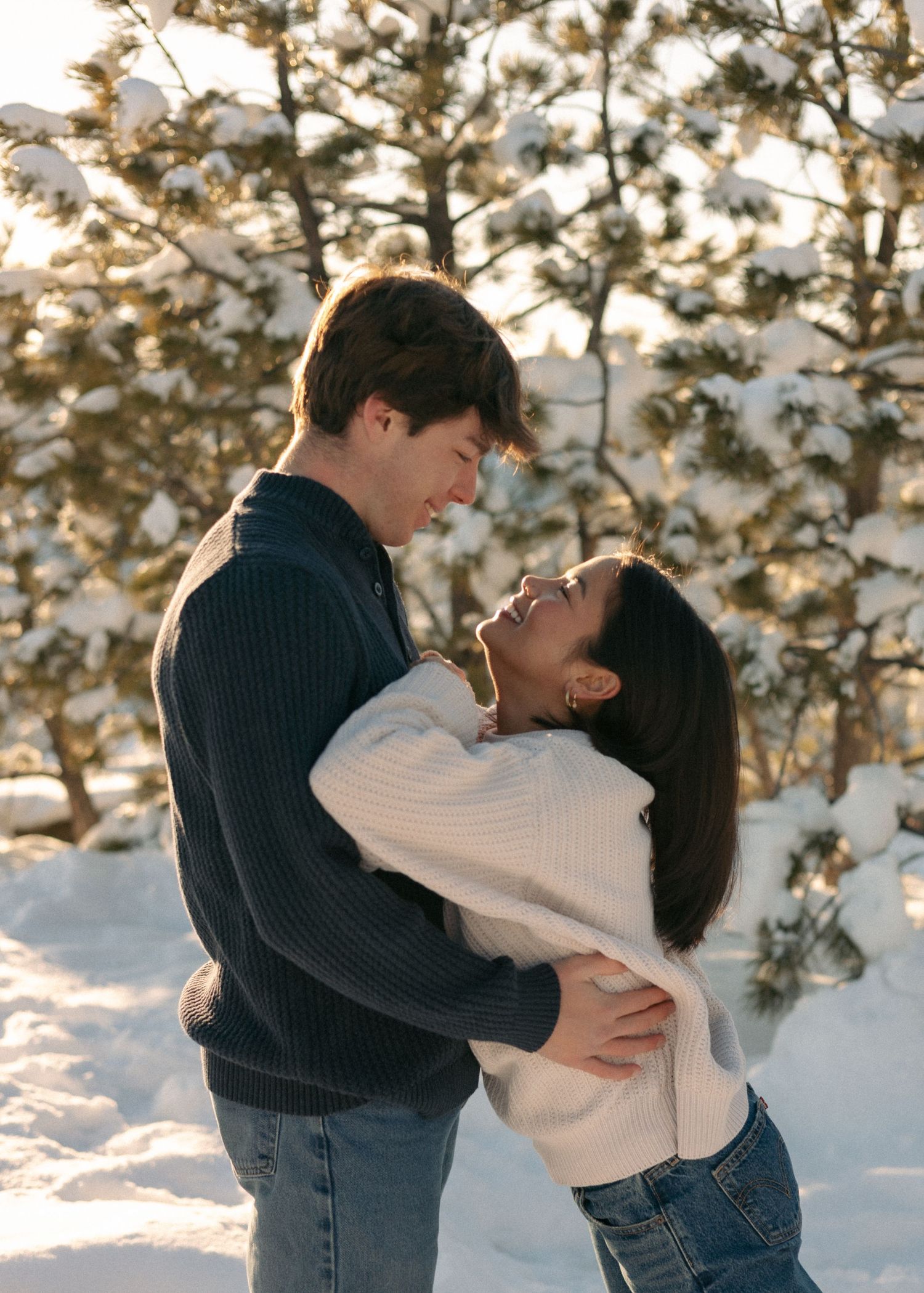 Romantic couple embracing and smiling at each other in sunny snowy pine forest.