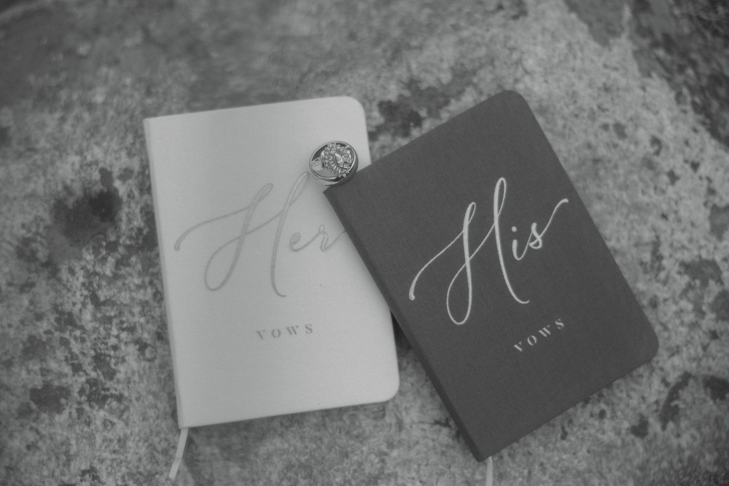 Black and white photo of His and Hers wedding vow books with a diamond ring resting on top.