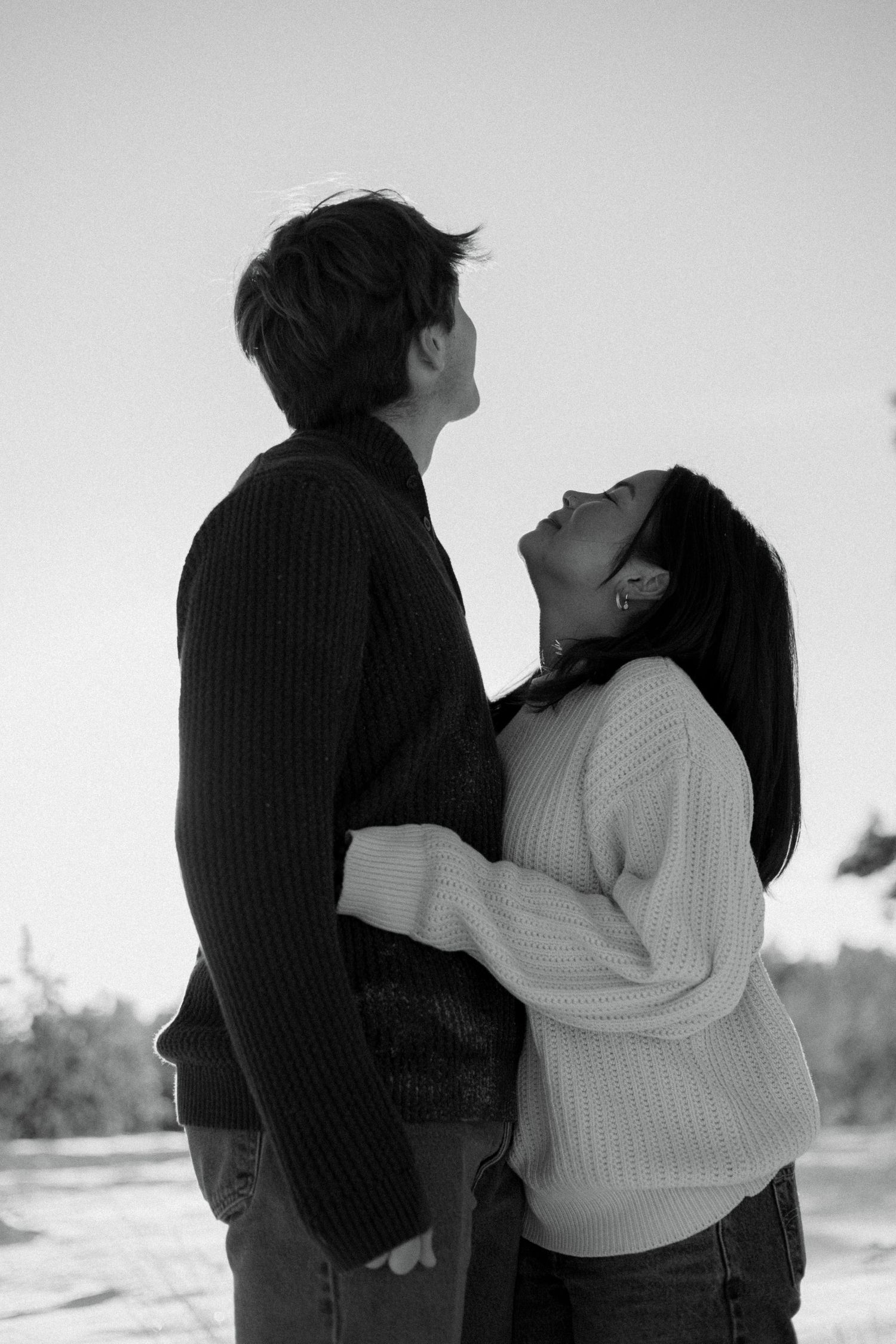 Black and white photo of a couple embracing and gazing at each other outdoors in winter.