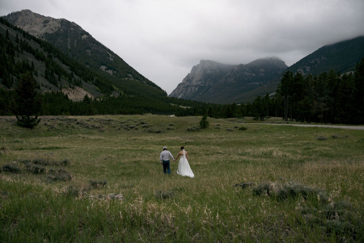Bride and groom walk through mountain meadow with misty peaks backdrop at Banff National Park wedding.